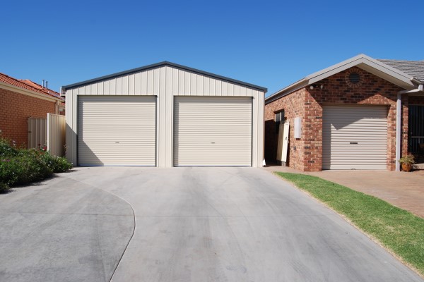 Cream coloured double steel garage pictured beside a red brick home with a concrete driveway