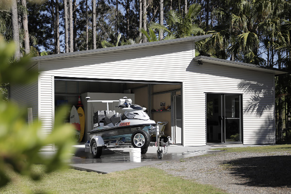 A skillion roof garage with a lean to and eave overhangs, with cleaning products pictured next to a jetski on a trailer parked outside