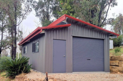 A smaller shed with a red skillion roof and grey walls, with a roller door and personal access door both in blue. 