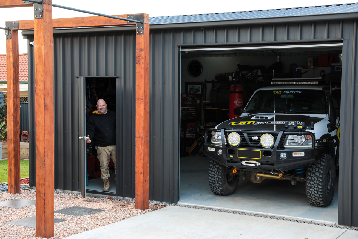 Man holding open the personal access door on his COLORBOND steel matt garage with a four wheel drive parked inside