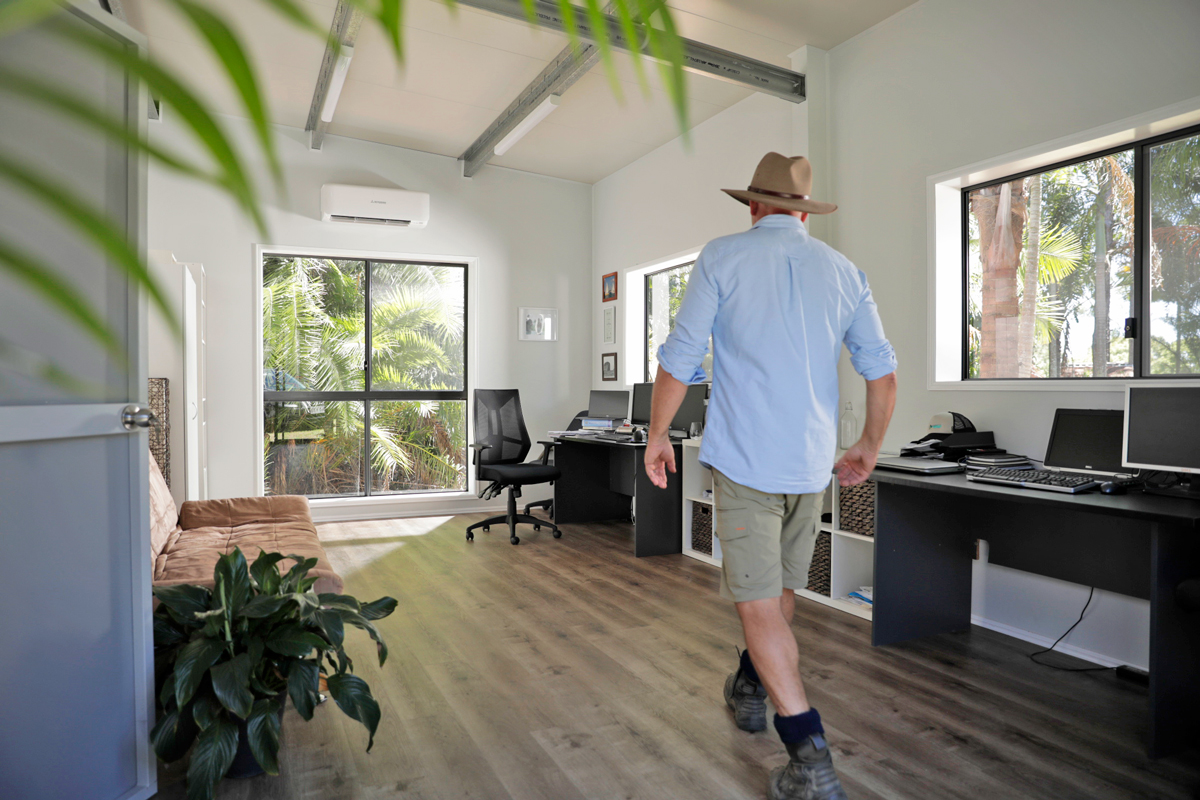 Man walking through a shed home office with plants and computers