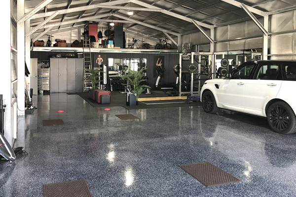 Internal shot of large shed with a parked white car, gym at the back and a mezzanine storage floor