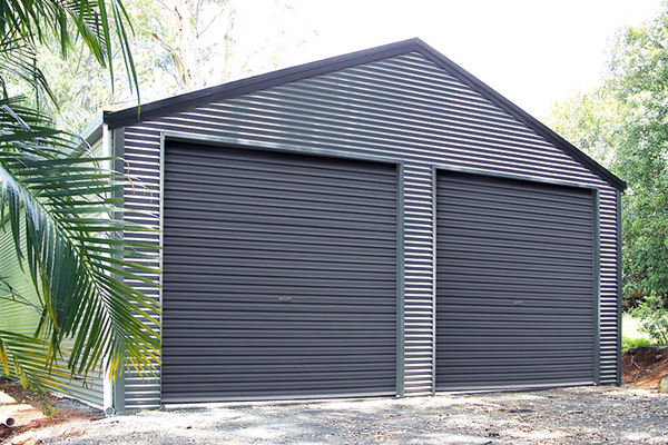 Grey shed with gable roof and two roller doors with palm fronds in foreground