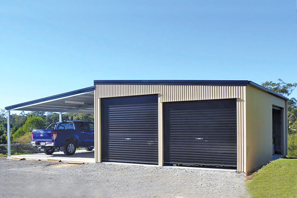 Cream shed with two black roller doors and open left lean-to with parked blue ute