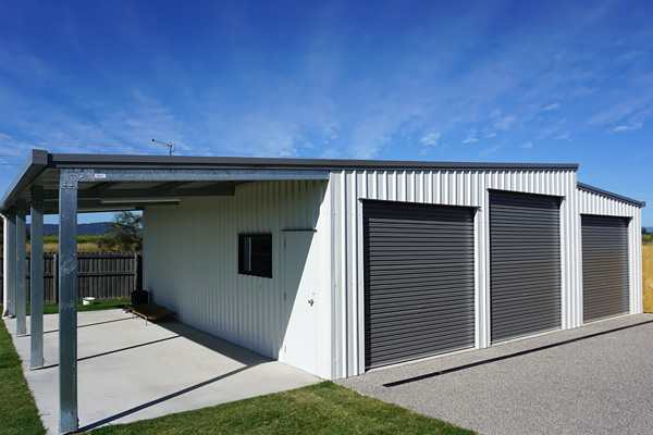 White shed with three grey roller doors and open awning on left side with white personal access door